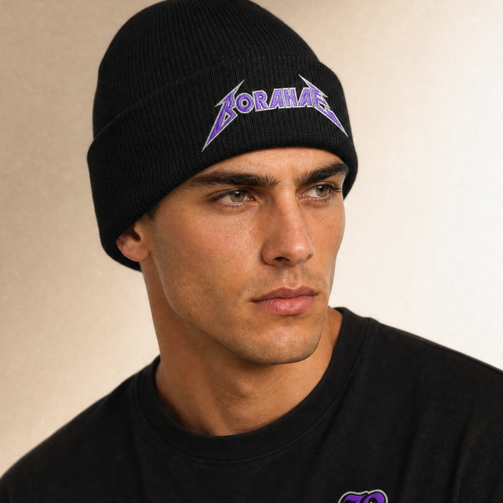 A close-up of a man wearing a black knit beanie with a purple and white 'Boromani' logo, paired with a black crewneck shirt against a warm beige background.